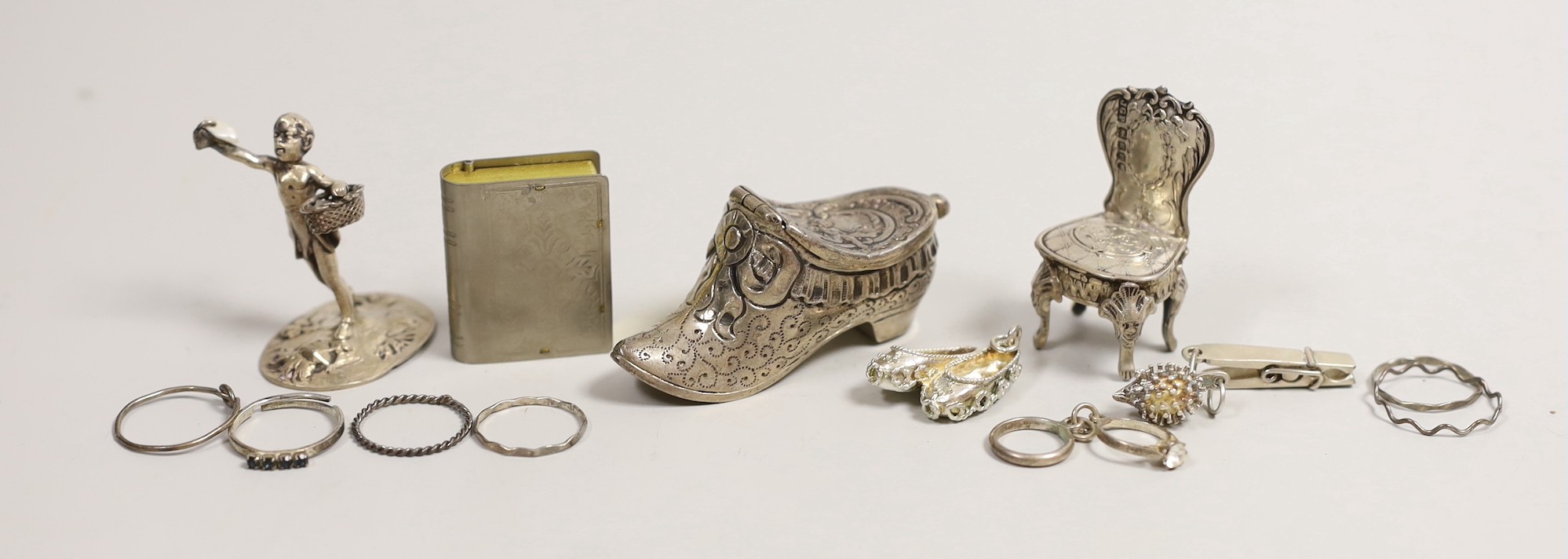 An Edwardian silver miniature model of an occasional chair, import marks for London, 1902, 43mm, a continental white metal model of a shoe and a similar model of a young child, a base metal 'book' box containing a rosary